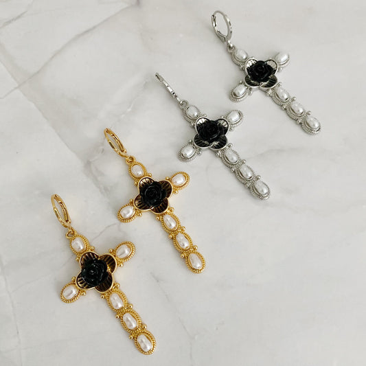 Two pairs of cross shaped  drop earrings, one with a gold plating and the other with a rhodium plating, each featuring faux pearls and a black rose motif.