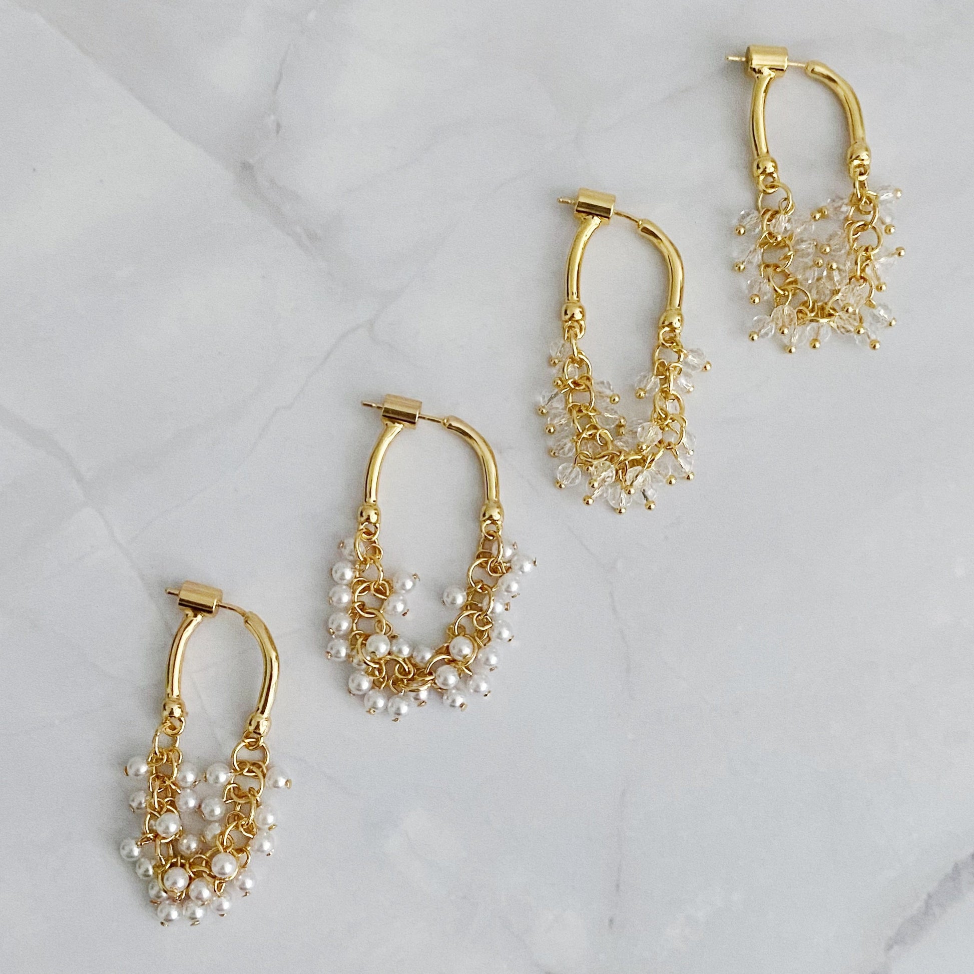 A set of two gold-colored hoop earrings with intricate bead designs, displayed on a marble surface.