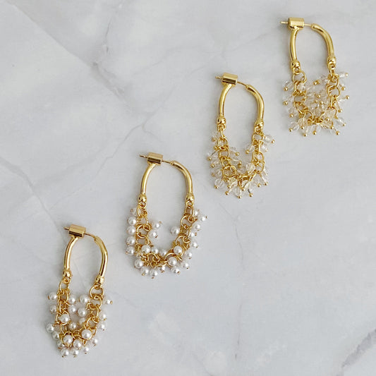 A set of two gold-colored hoop earrings with intricate bead designs, displayed on a marble surface.