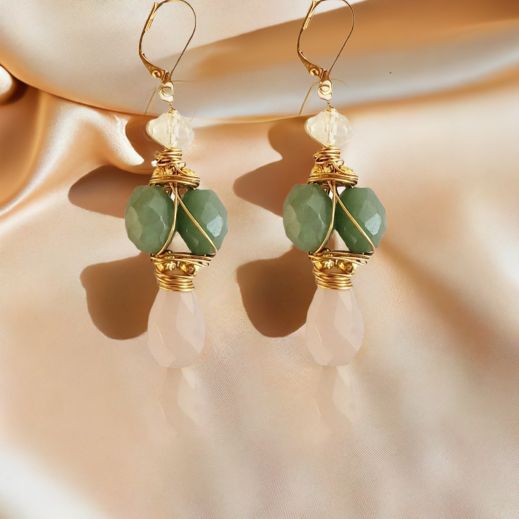 A pair of gold earrings featuring green aventurine and pink blush chalcedony stones, displayed against a satin backdrop.