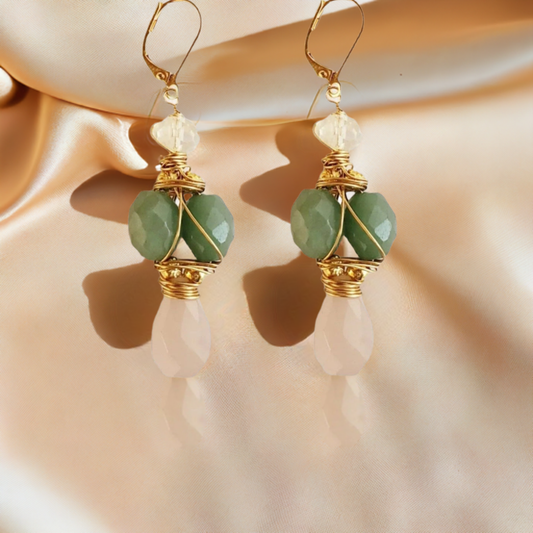 A pair of gold earrings featuring green aventurine and pink blush chalcedony stones, displayed against a satin backdrop.