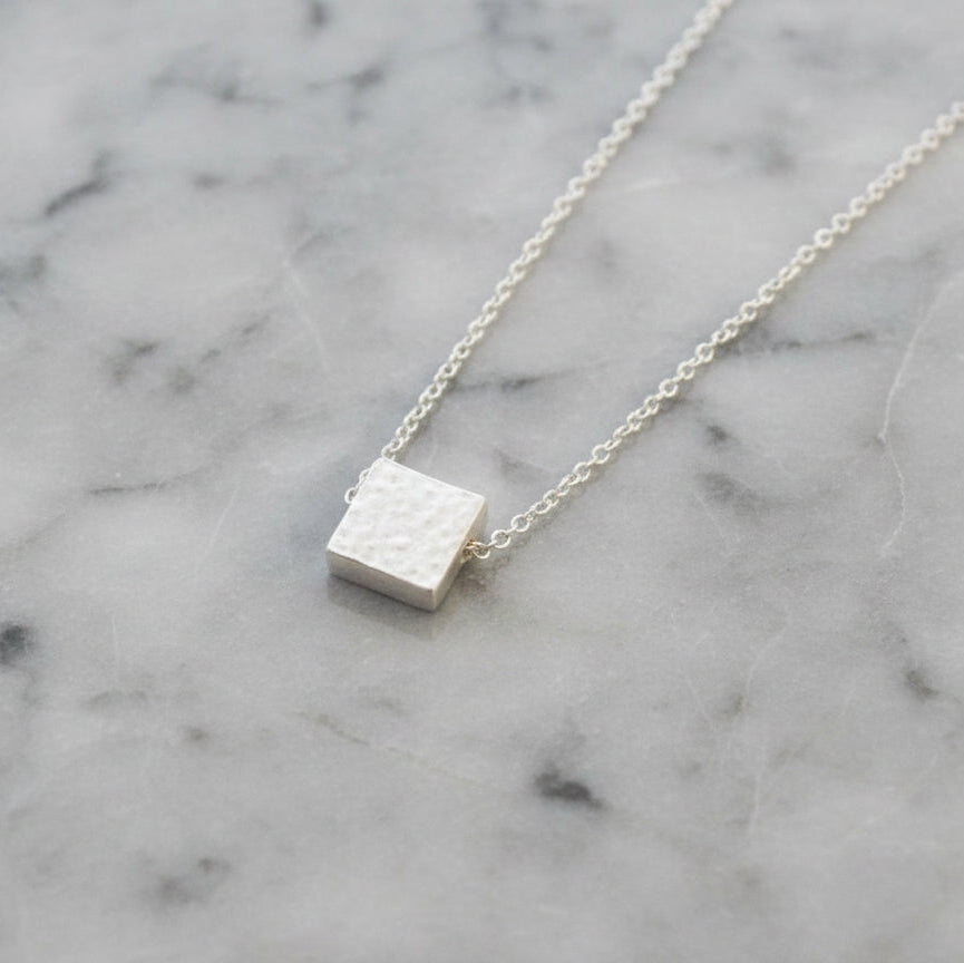 Silver square pendant necklace on a marble surface