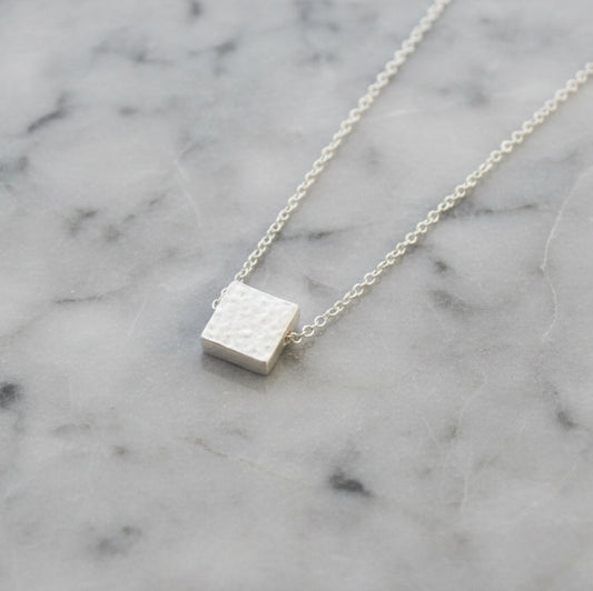 Silver square pendant necklace on a marble surface