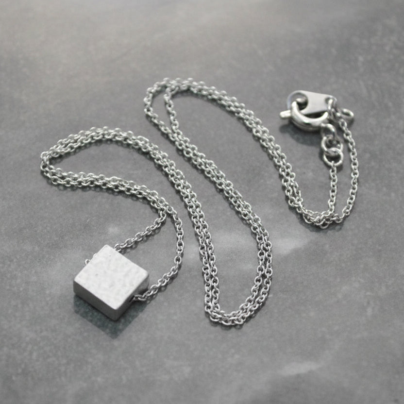 Silver necklace with a square pendant on a gray surface