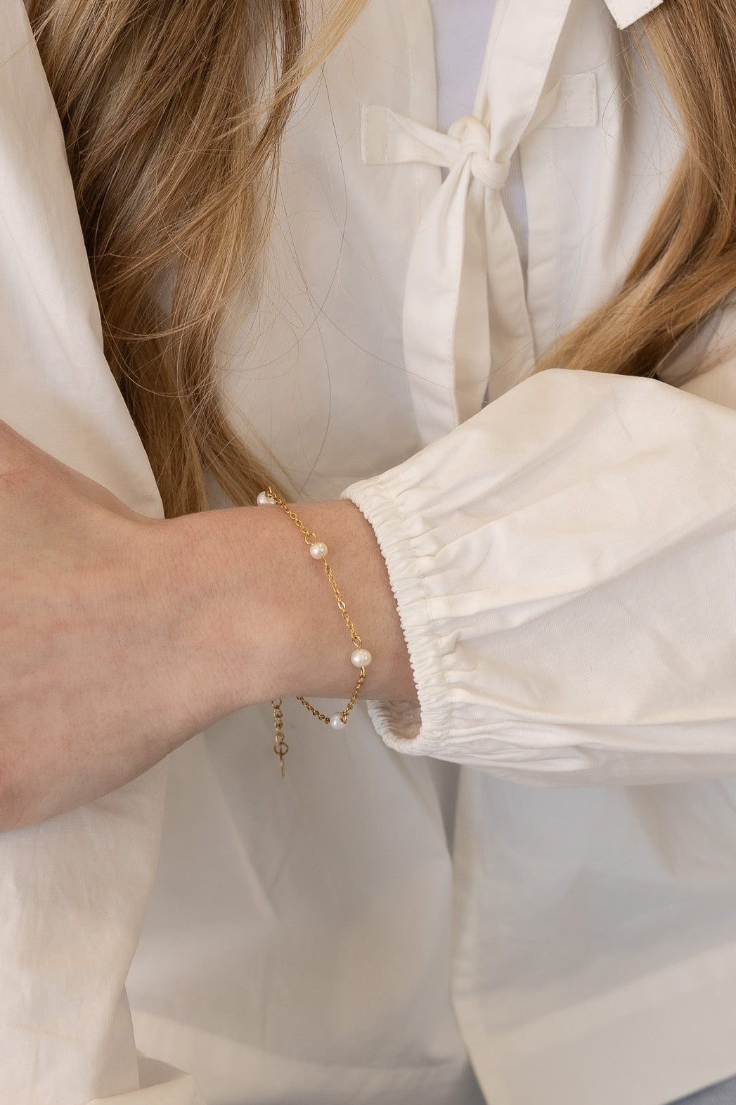 Person wearing a white blouse with puffed sleeves and a pearl bracelet.