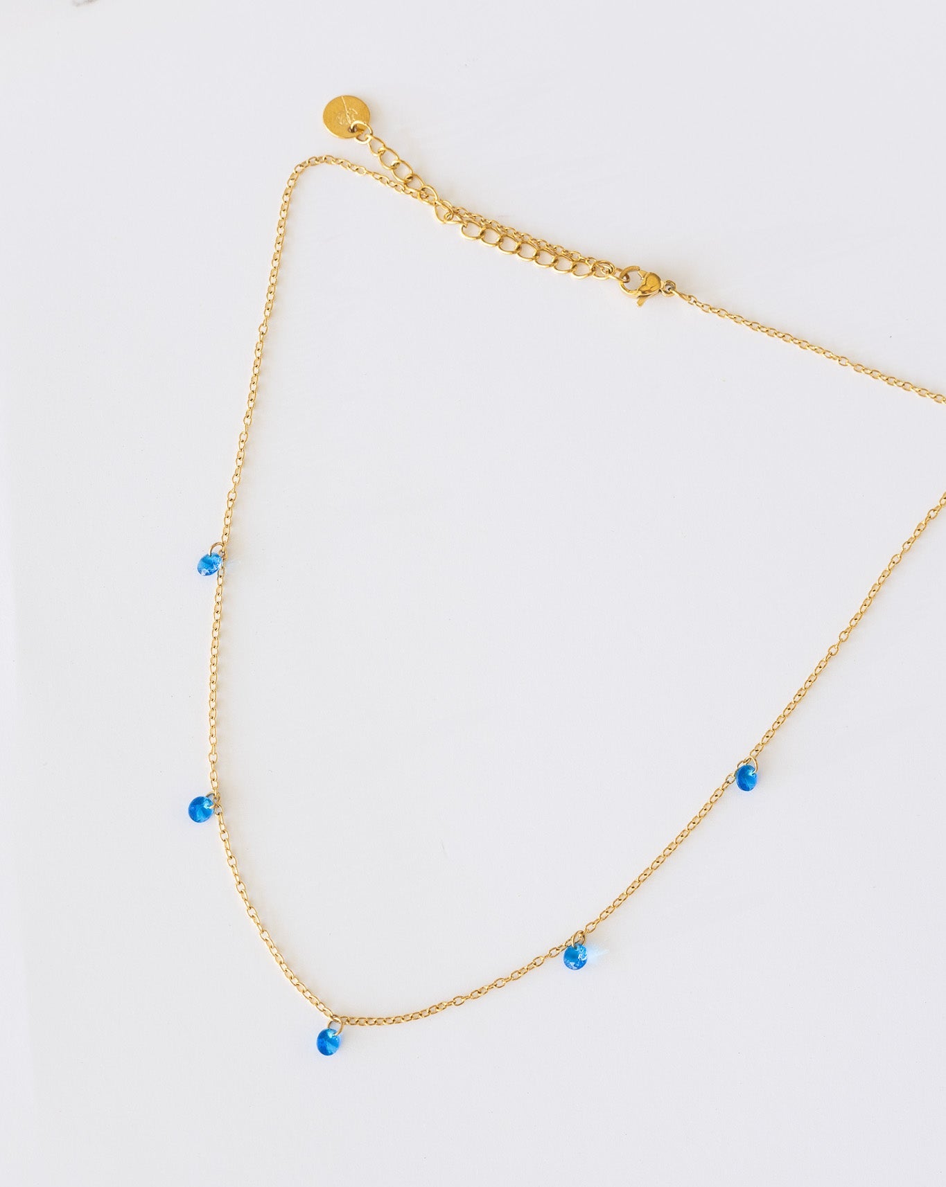 Gold necklace with blue beads on a light gray background