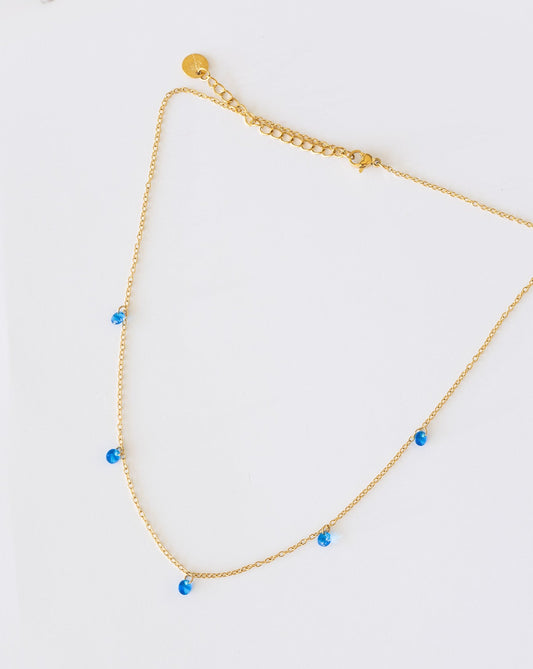 Gold necklace with blue beads on a light gray background