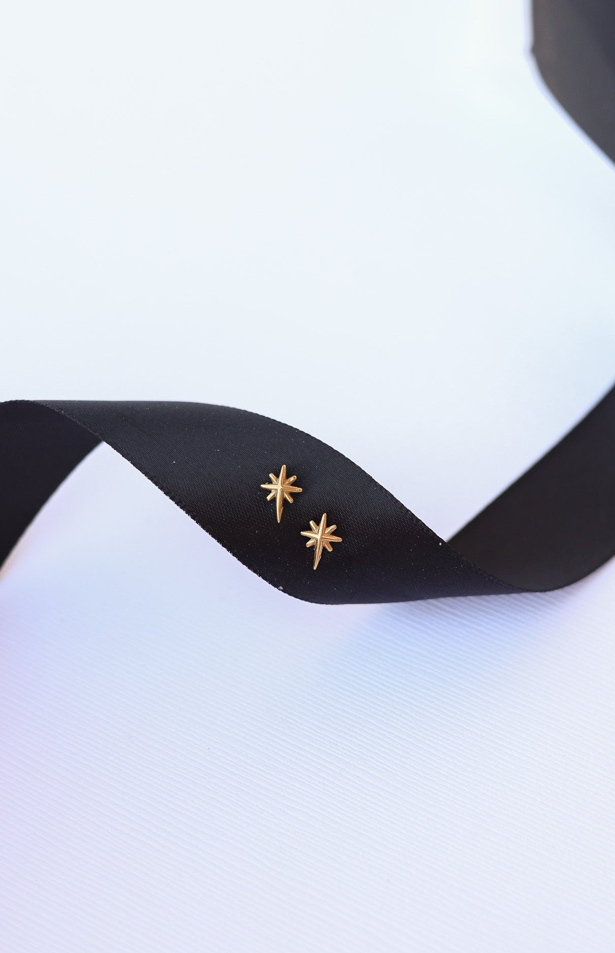 Gold star-shaped earrings on a black ribbon with a white background