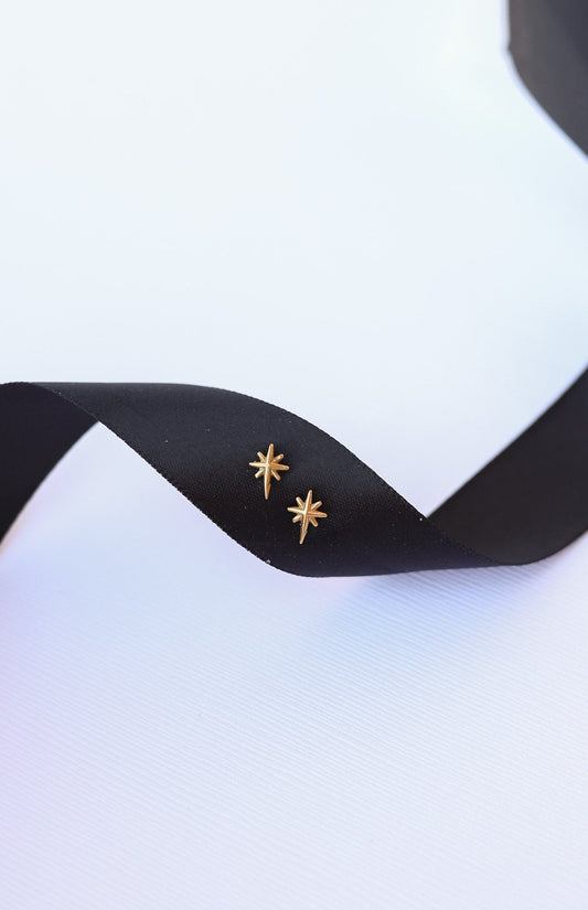 Gold star-shaped earrings on a black ribbon with a white background