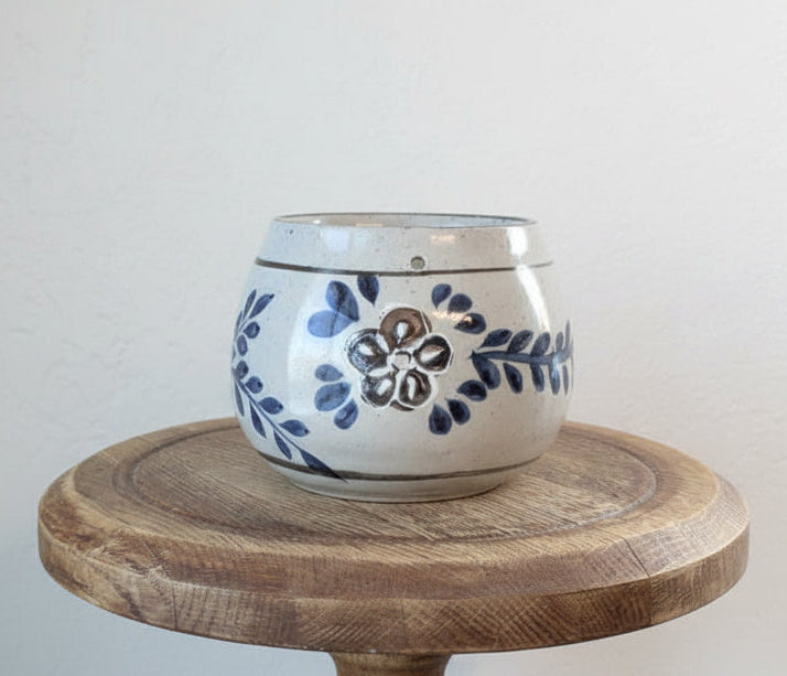 Ceramic pot with blue floral design on a wooden stand against a plain background