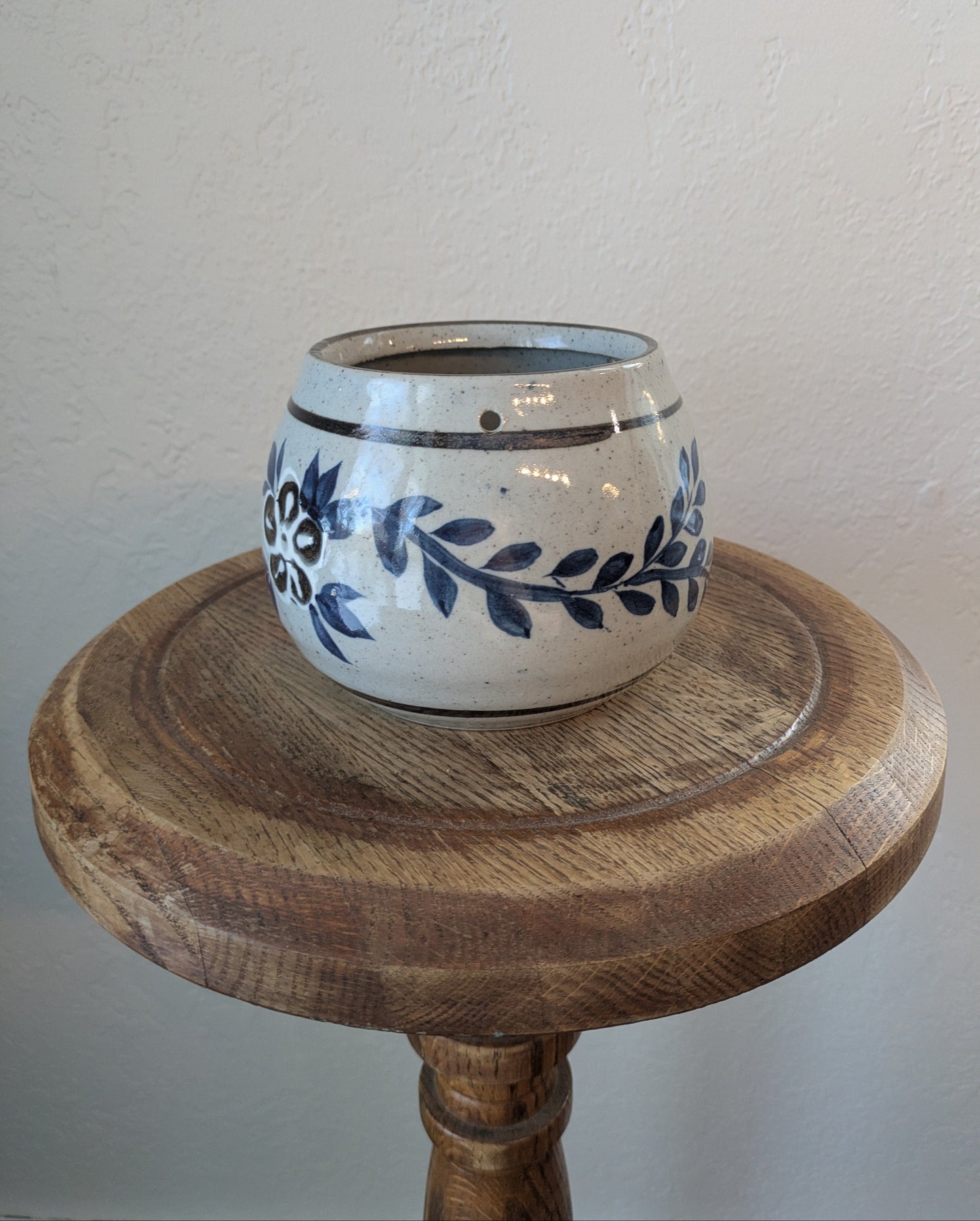 Ceramic pot with blue floral design on a wooden stand against a plain wall