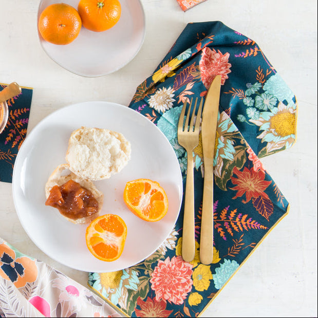 Breakfast setting with biscuits, jam, and oranges on a floral tablecloth.
