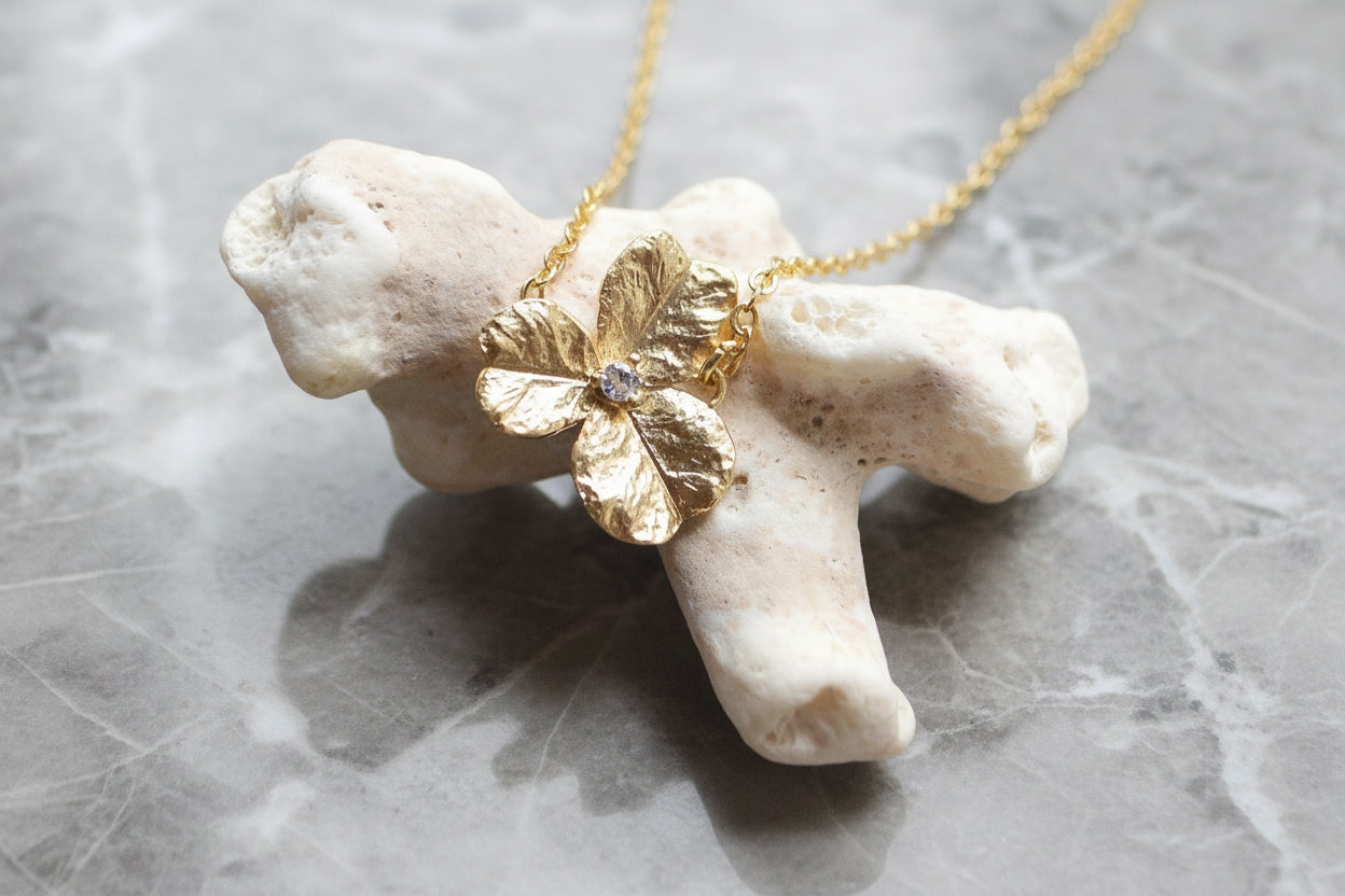 Gold flower pendant necklace on a piece of coral with a gray background
