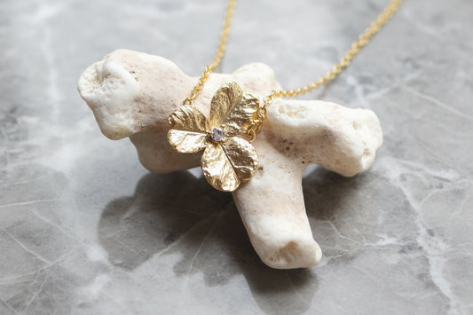 Gold flower pendant necklace on a piece of coral with a gray background