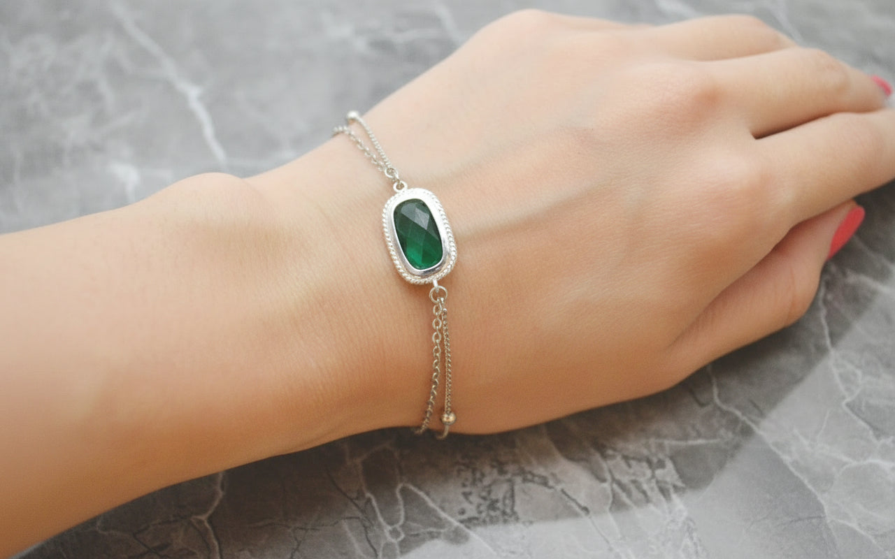 Hand wearing a bracelet with a green gemstone on a dark surface