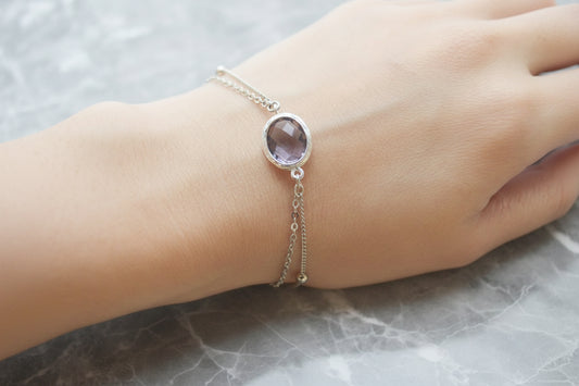 Close-up of a hand wearing a silver bracelet with a purple gemstone on a dark surface.